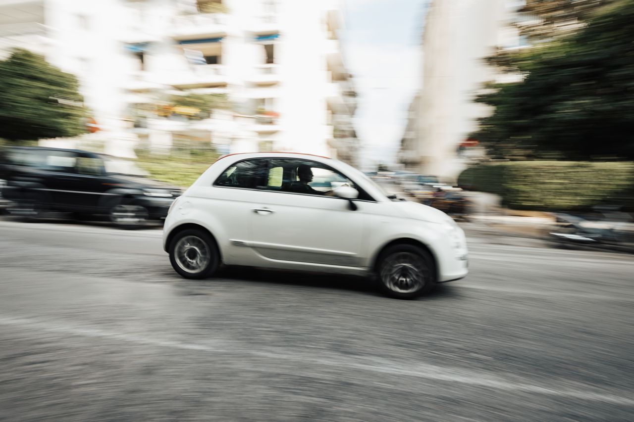 Dynamic capture of a compact white car speeding through a city street with motion blur effect.