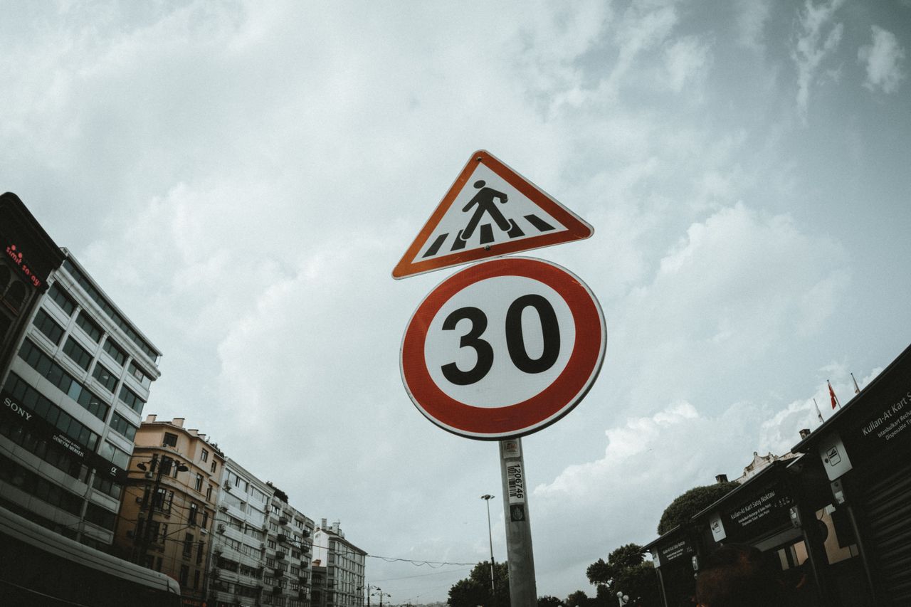 Low-angle view of pedestrian and speed limit signs against a cloudy sky in an urban setting.