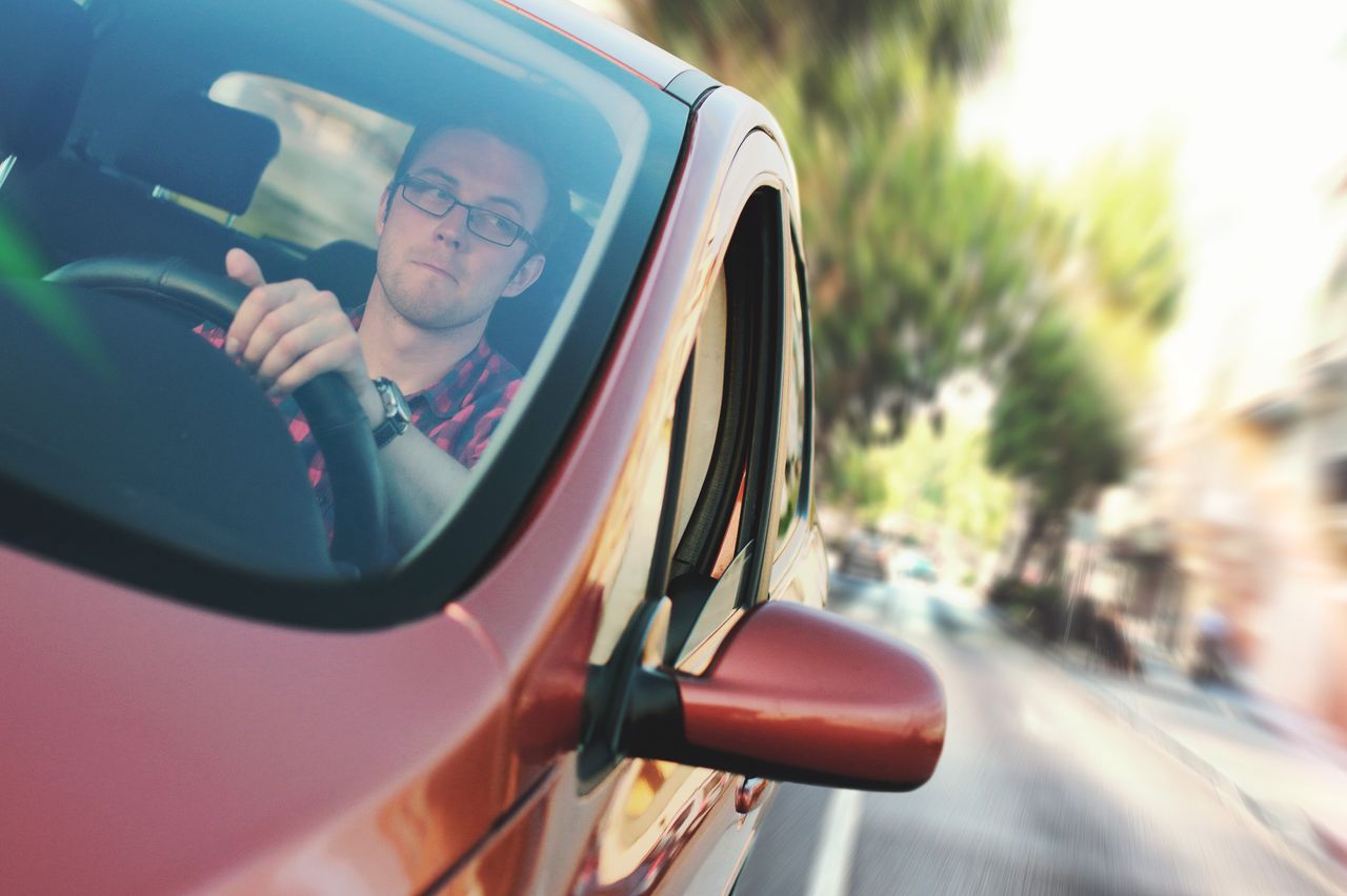 A man driving fast through a city street in a red car, showcasing motion and focus.