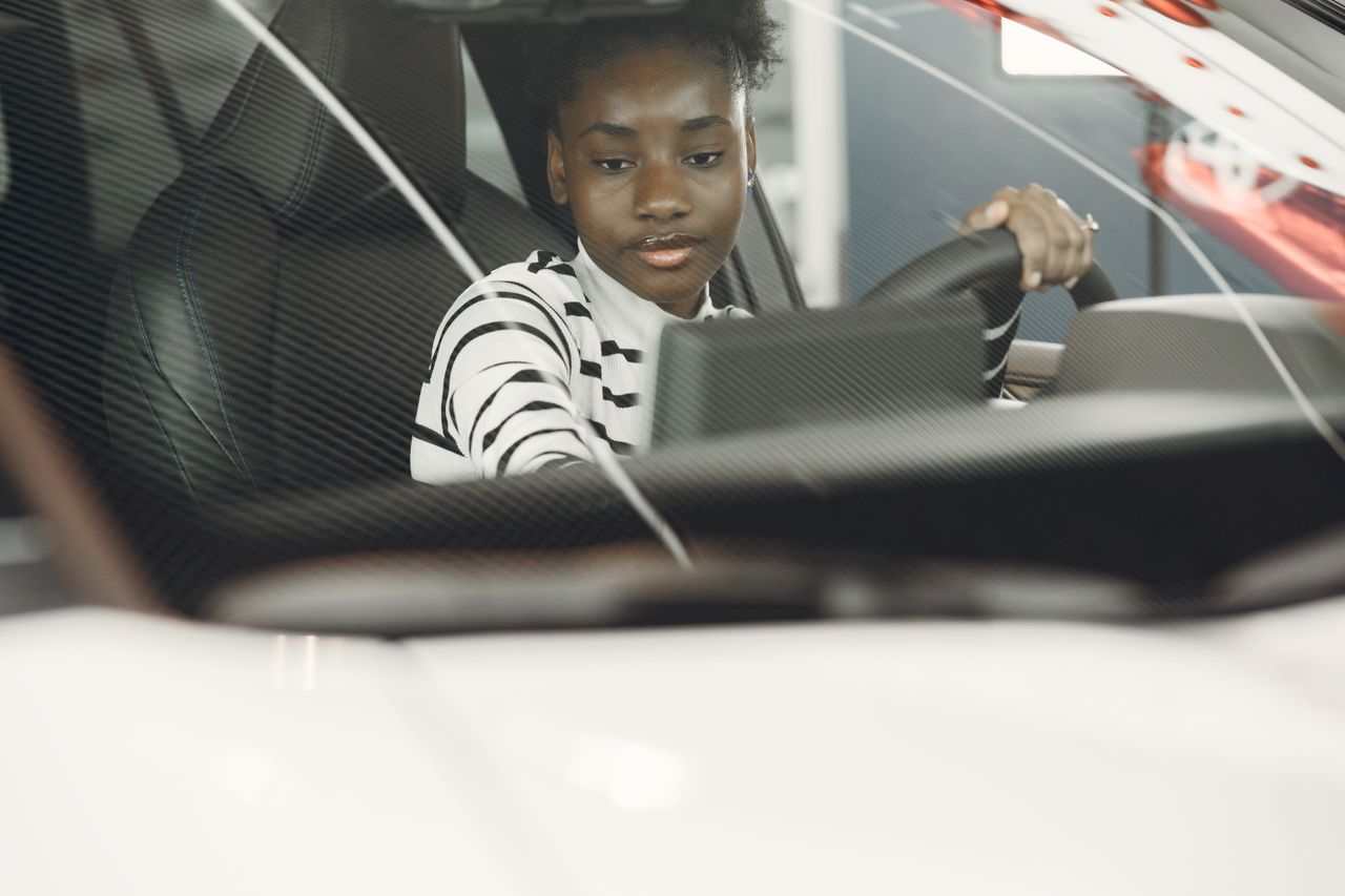 Crafting Captivating Headlines: Your awesome post title goes here Young woman with black hair driving a car, captured from the interior with focus on the steering wheel.